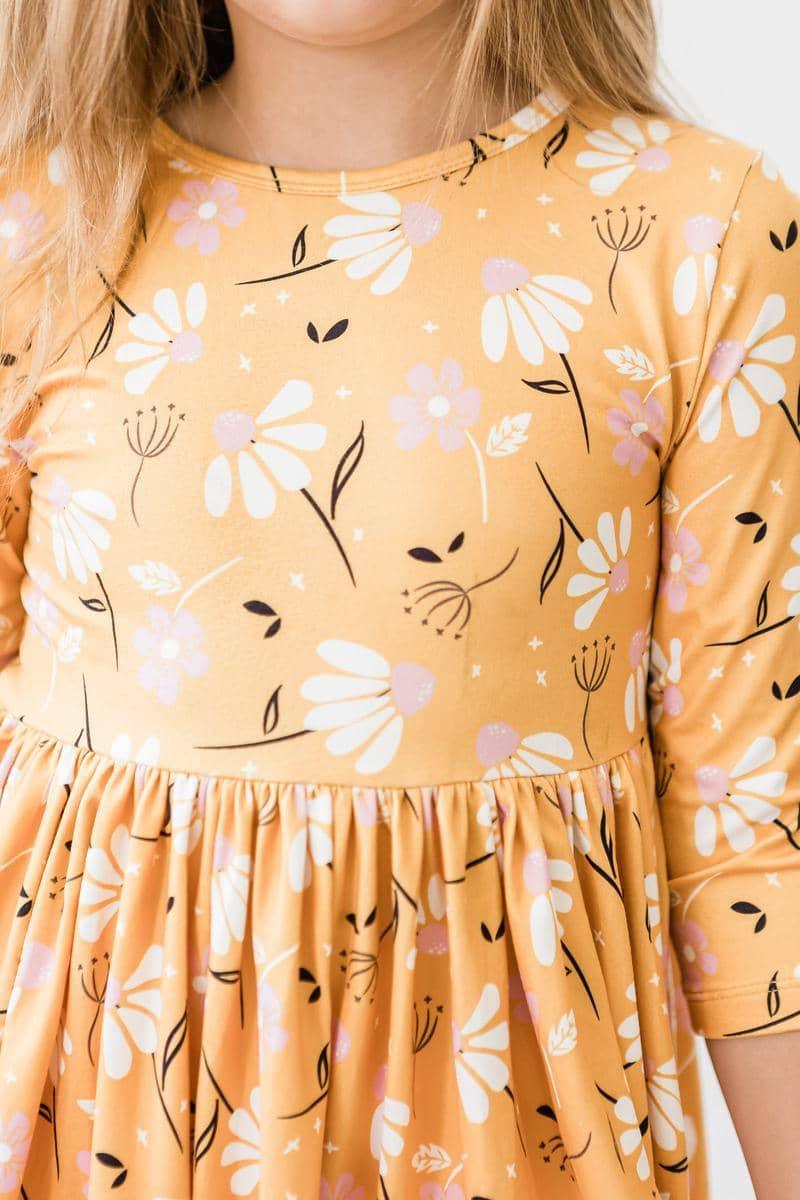 Girl wearing mustard yellow dandelion twirl dress for girls with white and pink floral print standing still