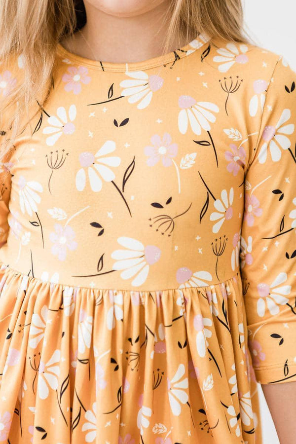 Girl wearing mustard yellow dandelion twirl dress for girls with white and pink floral print standing still