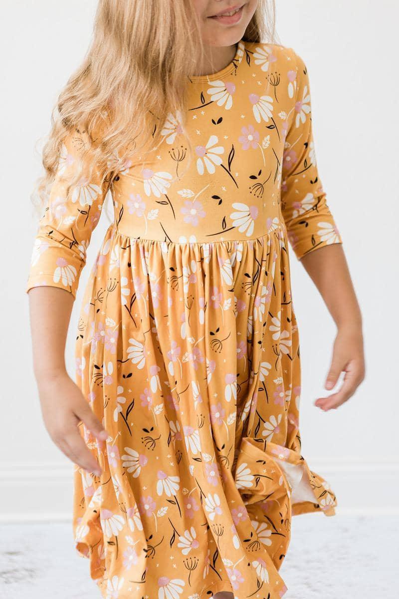 Girl wearing dandelion twirl dress for girls in yellow with white floral print holding skirt while spinning