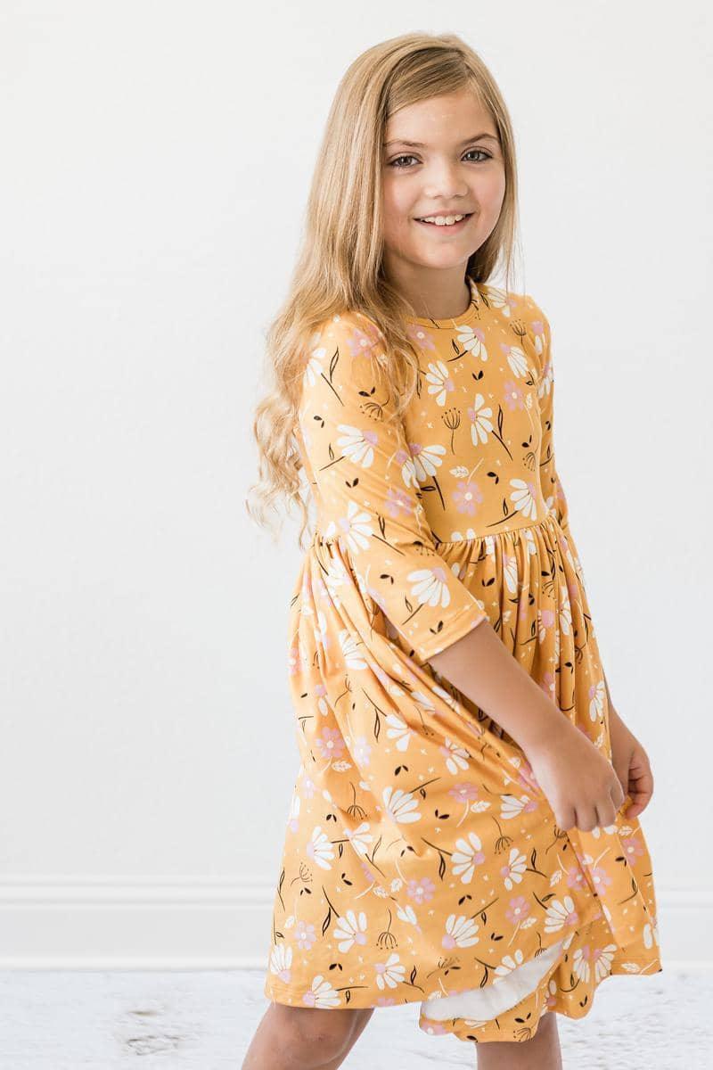 Young girl wearing dandelion twirl dress for girls in mustard yellow with floral print smiling and posing