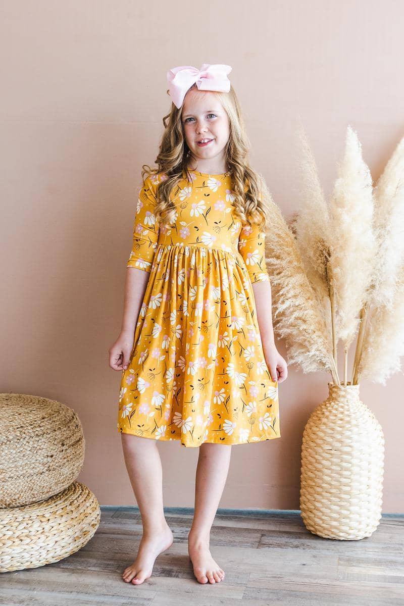 young girl wearing yellow dandelion twirl dress for girls with 3/4 sleeves smiling indoors