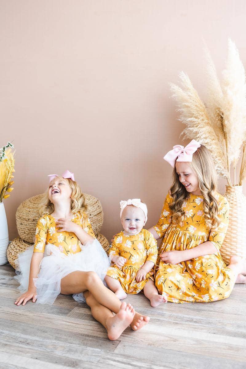 Three girls wearing dandelion twirl dress for girls in yellow smiling and sitting on floor playing