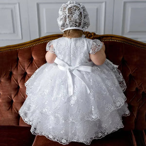 baby girl wearing delicate lace baptism gown for baby girls with bonnet sitting on brown vintage sofa