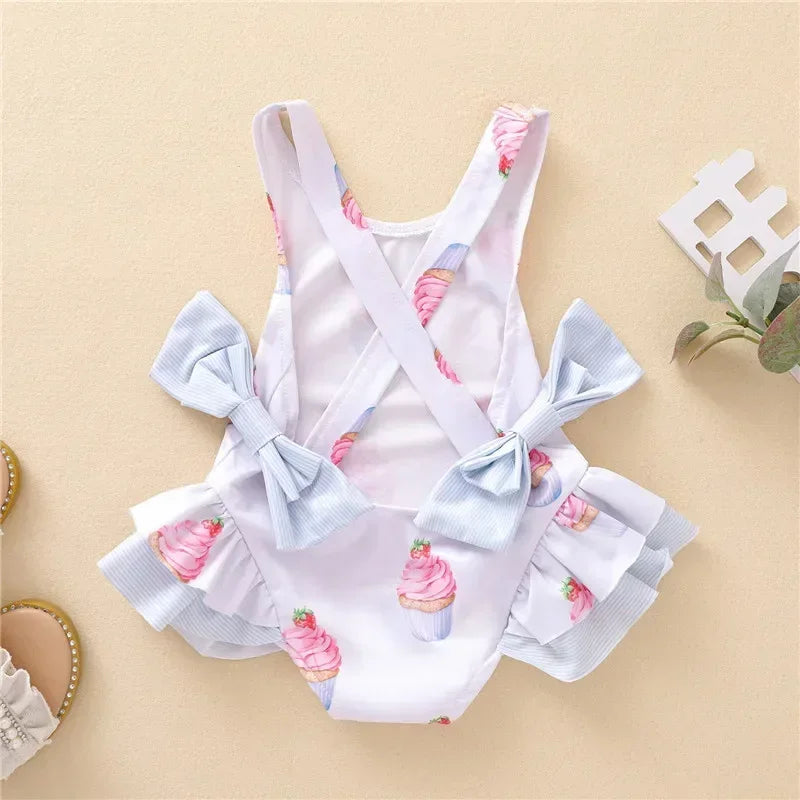 White dessert themed baby swimsuit with pink cupcake prints and blue ruffle bows for infants
