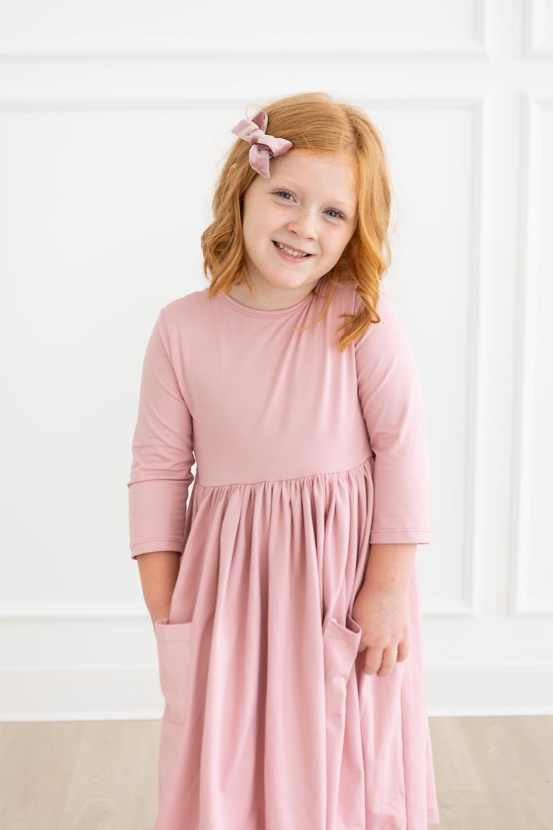 A young girl happily modeling the Vintage Pink 3/4 Sleeve Pocket Twirl Dress from Mila & Rose, highlighting its soft and stylish look.