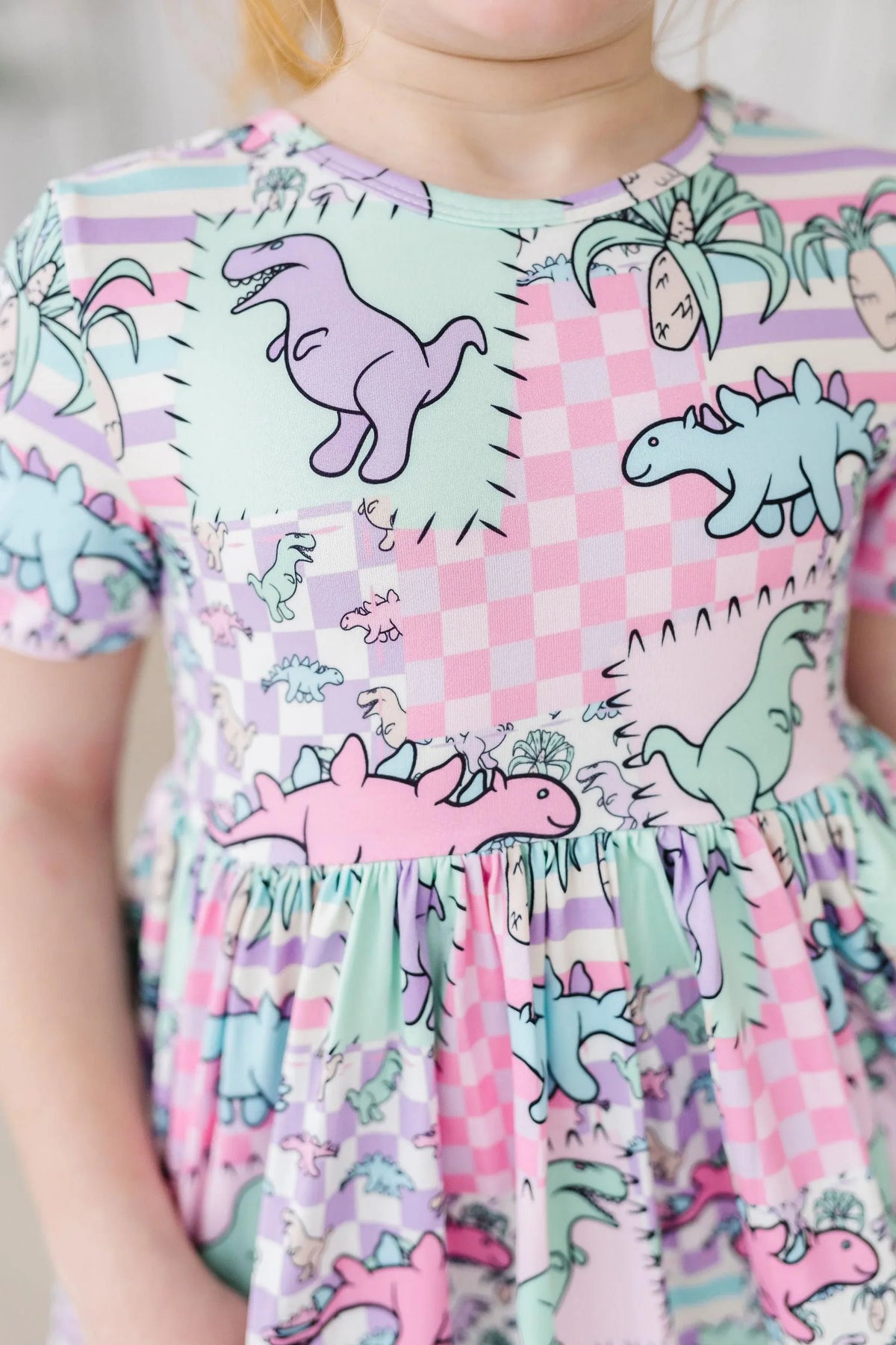 young girl wearing pastel dinosaur twirl dress for girls with pink and mint colors standing still