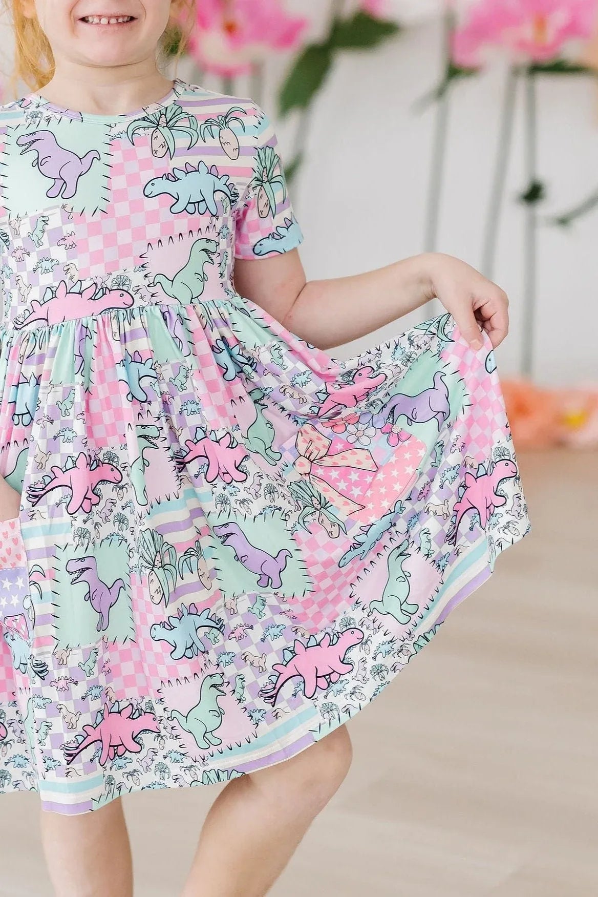 Girl wearing pastel dinosaur twirl dress for girls with short sleeves holding skirt out