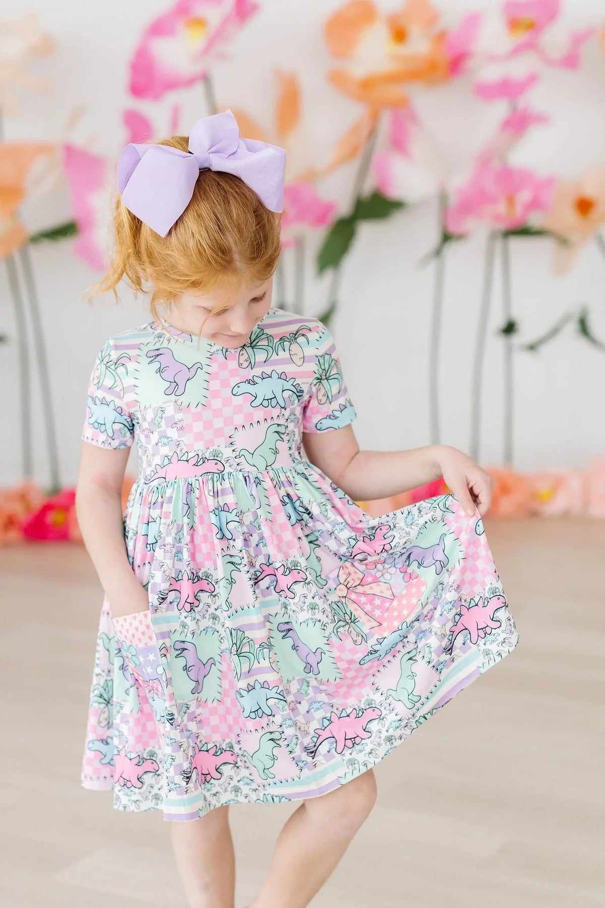 Young girl wearing pink and mint dinosaur twirl dress for girls with short sleeves holding skirt out