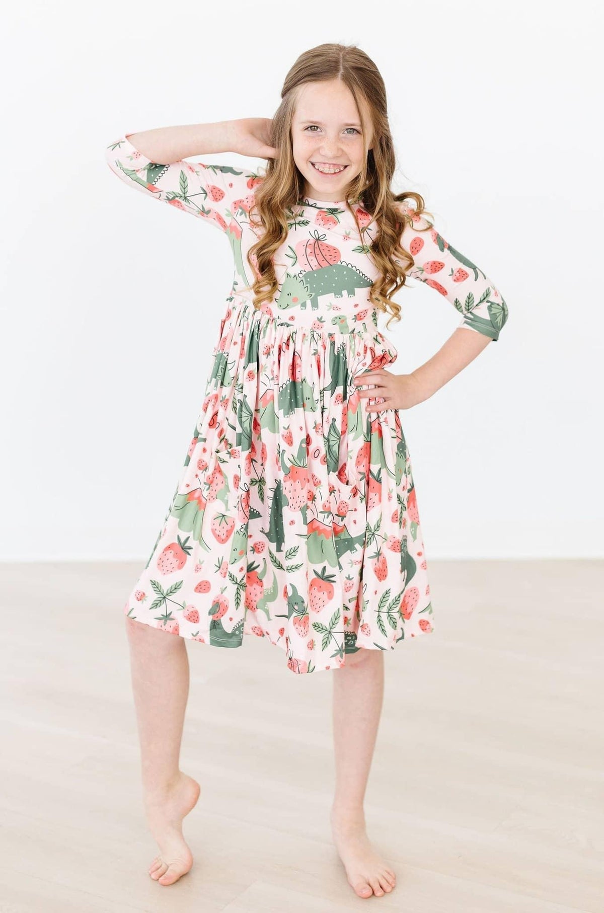 girl wearing dinosaur twirl dress for girls in pink and green with 3/4 sleeves smiling and posing with hand on hip