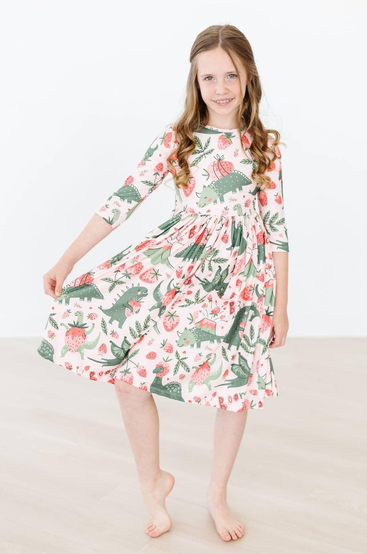 Young girl wearing dinosaur twirl dress for girls in white with green and pink dinosaurs posing with dress flared out