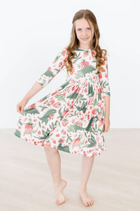 Young girl wearing dinosaur twirl dress for girls in white with green and pink dinosaurs posing with dress flared out