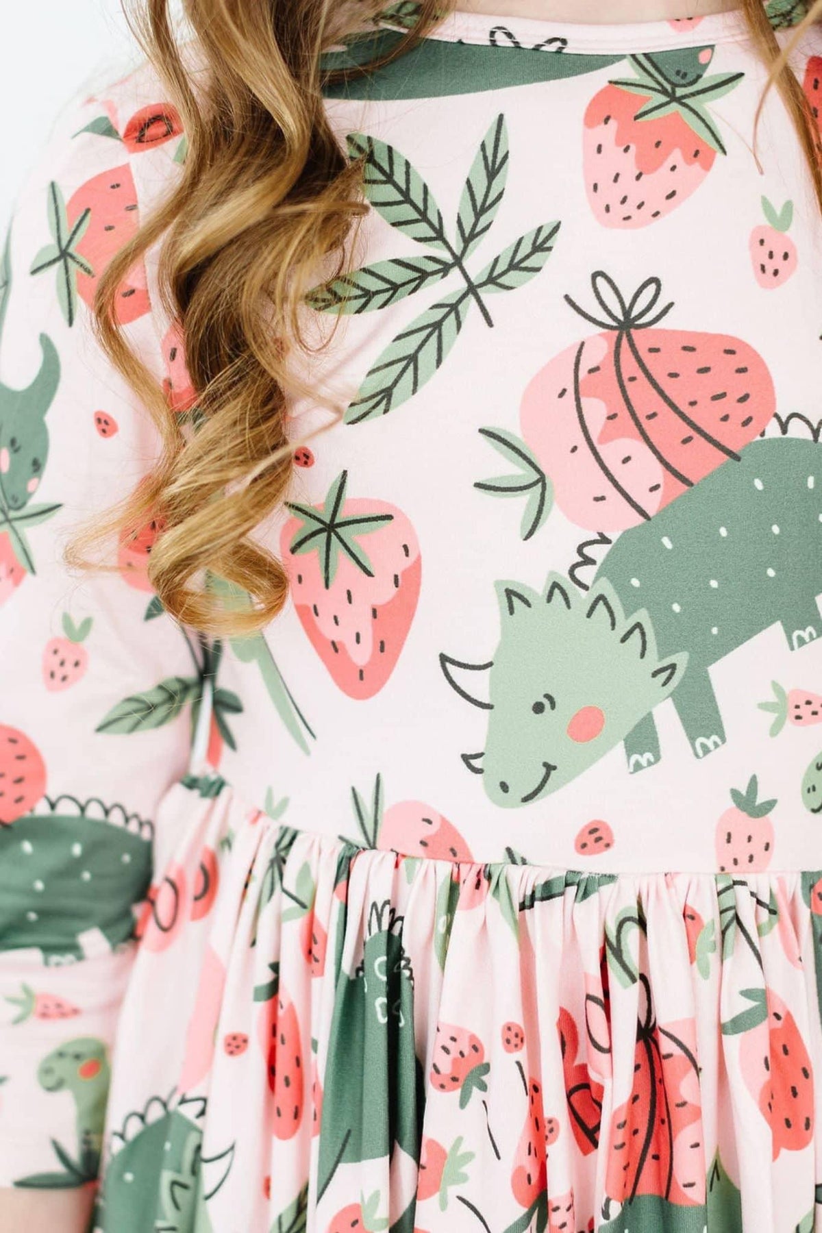 close-up of girl wearing pink dinosaur twirl dress for girls with strawberries and leaves print