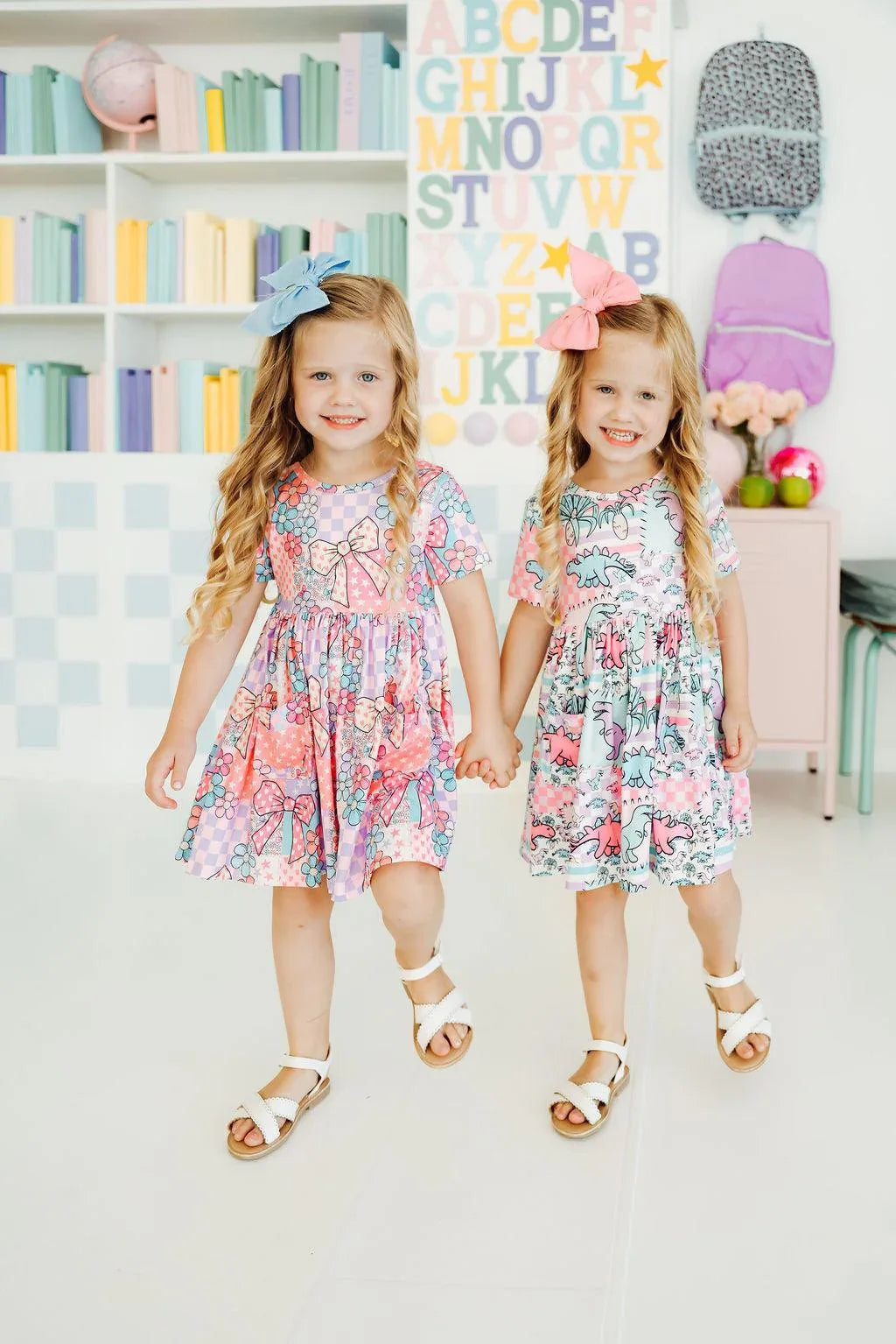 Two young girls wearing colorful dinosaur twirl dress for girls holding hands and smiling indoors