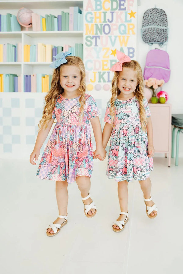 Two young girls wearing colorful dinosaur twirl dress for girls holding hands and smiling indoors