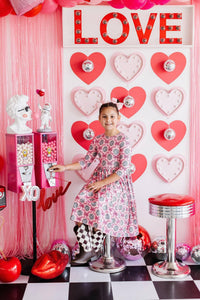 Girls pink floral disco bow twirl dress for girls with 3/4 sleeves by Mila & Rose sitting in retro themed room