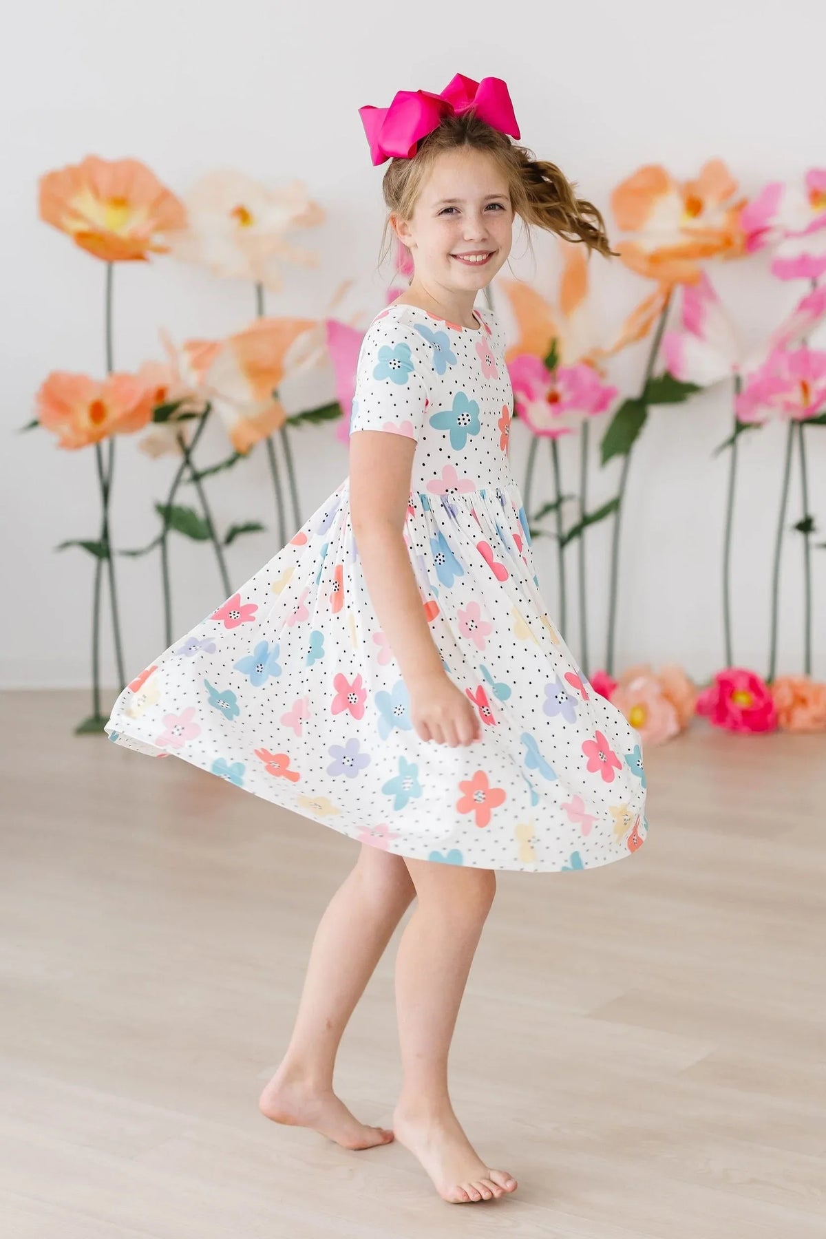 Young girl twirling in a white dots and daisies pocket dress for girls with colorful flowers and a bright pink bow
