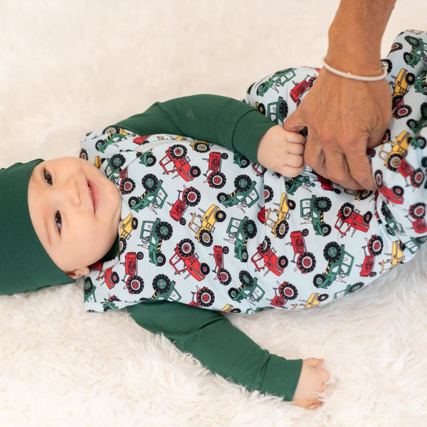 Baby lying on a blanket with a tractor pattern, wearing a green outfit.