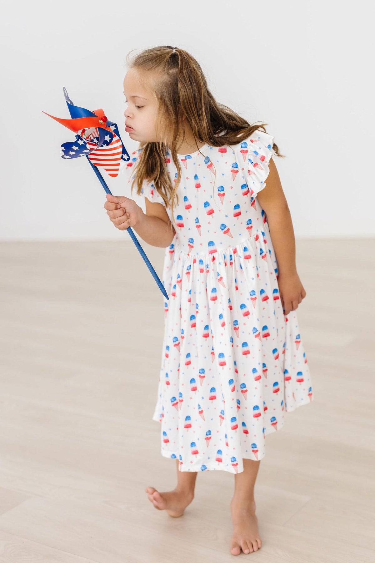 Girls white twirl dress flutter with red and blue summer print holding patriotic pinwheel dress for the summer