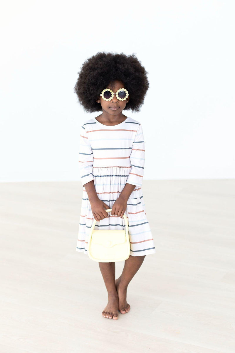 A stylish girl in the Fall Stripes 3/4 Sleeve Pocket Twirl Dress, holding a yellow handbag. She is wearing stylish flower-shaped sunglasses, showcasing a fun, fashionable look perfect for playdates or special occasions.