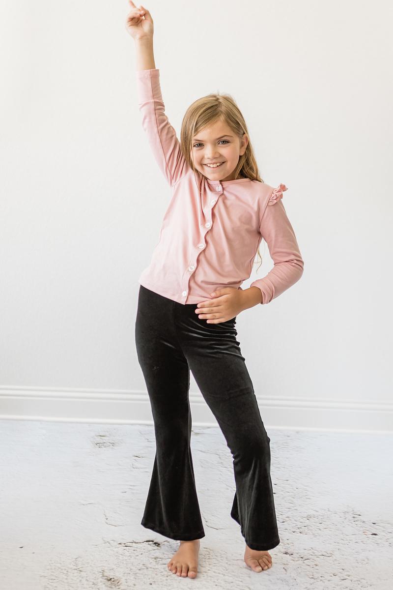A happy child striking a pose in Black Velvet Bells, paired with a pink top, demonstrating the versatility and chic style of these elegant velvet pants.