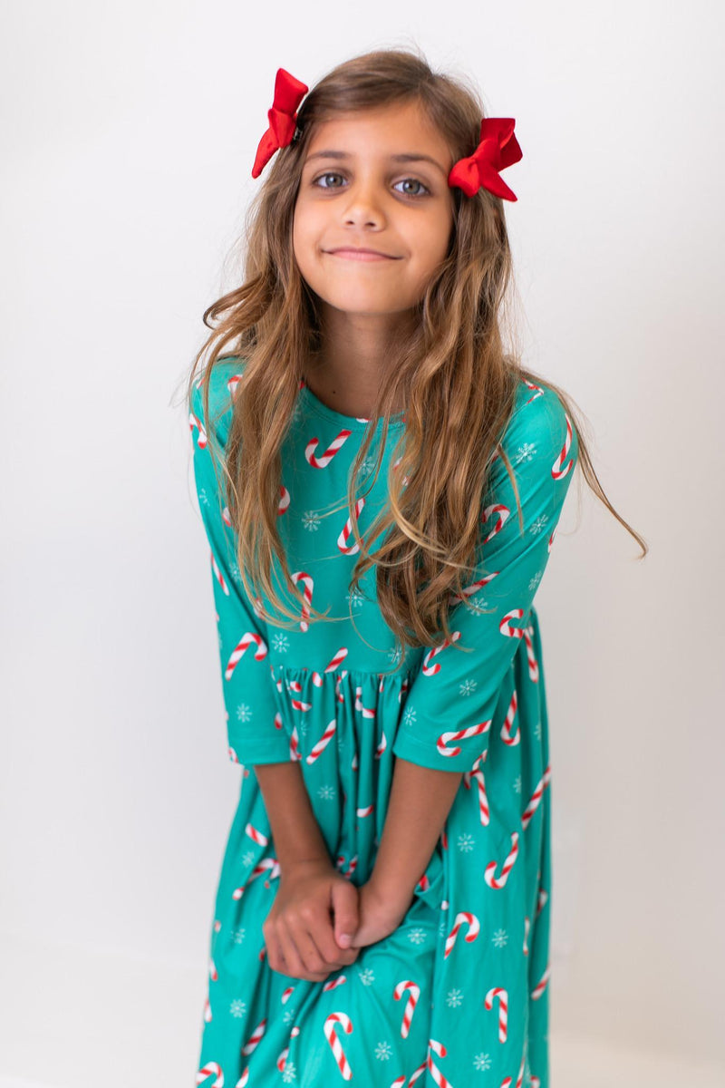 A smiling girl modeling the Christmas Candy 3/4 Sleeve Pocket Twirl Dress by Mila & Rose, featuring a fun candy cane design and cozy 3/4 sleeves.