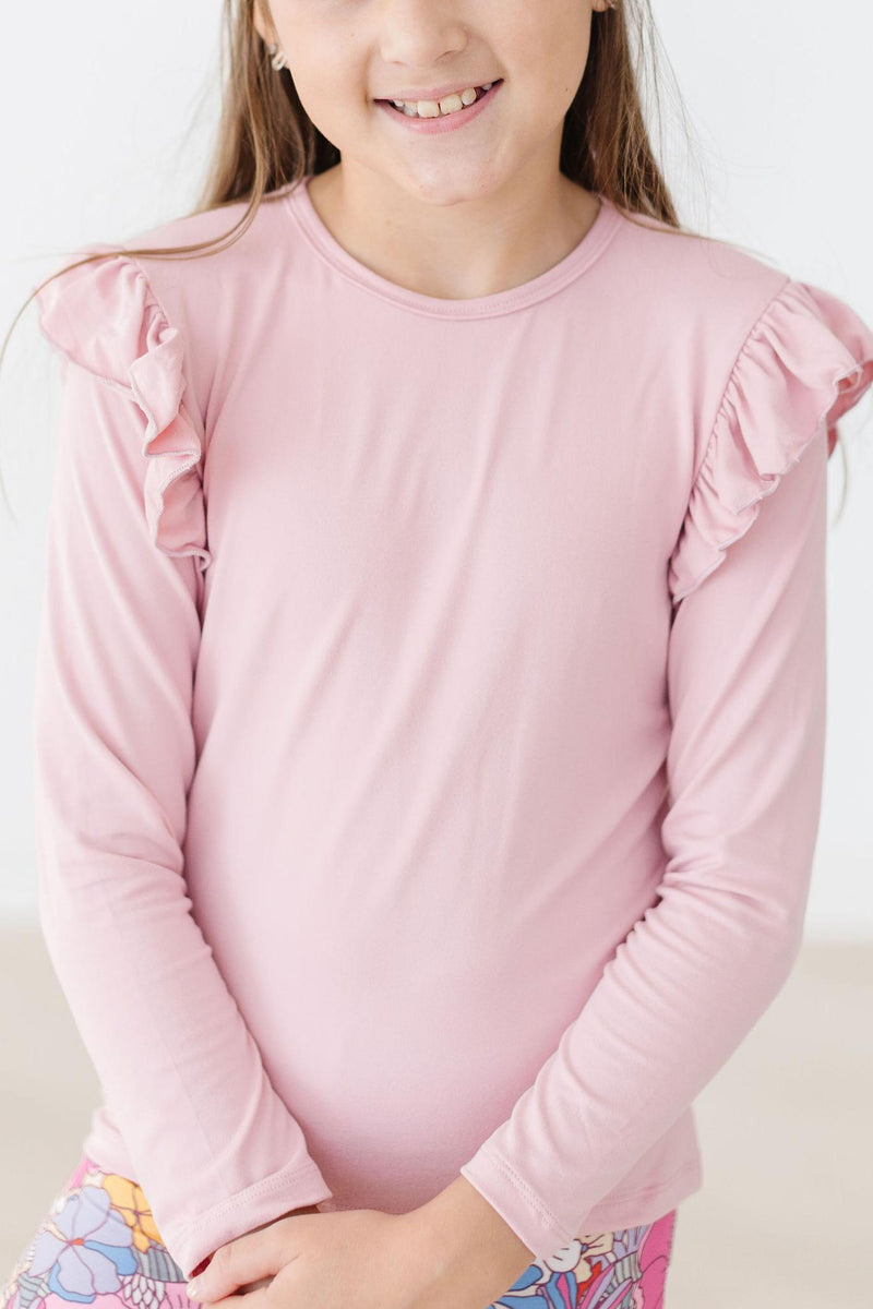 A smiling girl wearing the Vintage Pink Long Sleeve Ruffle Tee, showcasing the adorable ruffle details and soft pink color, perfect for adding vintage charm to any outfit.