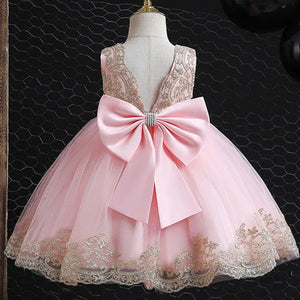 pink elegant baby girl party dress with gold lace and large bow on dress form