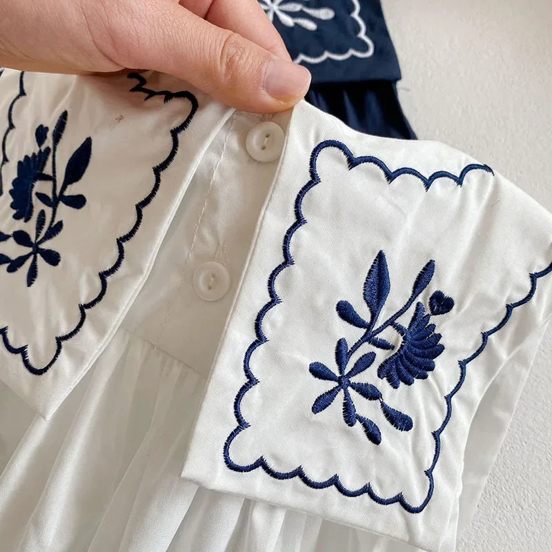 White embroidered baby romper with sailor collar for infants featuring navy blue floral embroidery detail