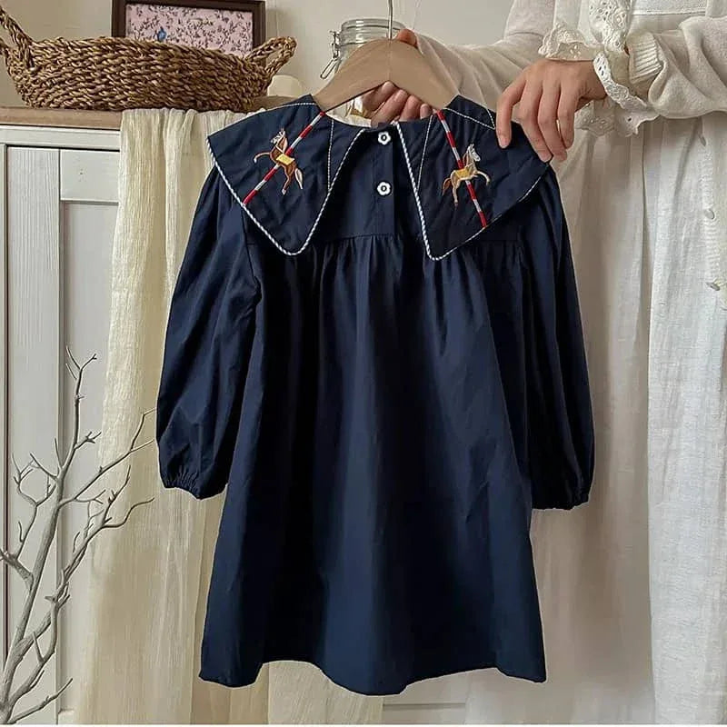 person holding navy blue embroidered dress for little girls with horse designs on collar