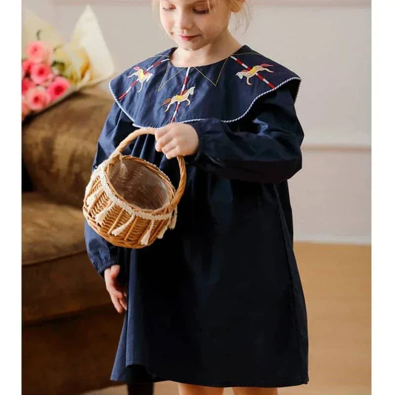 Little girl wearing navy embroidered dress for little girls holding a wicker basket indoors