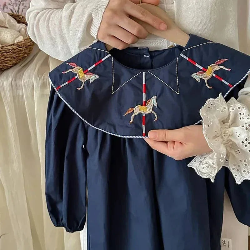 person holding navy embroidered dress for little girls with horse designs on collar