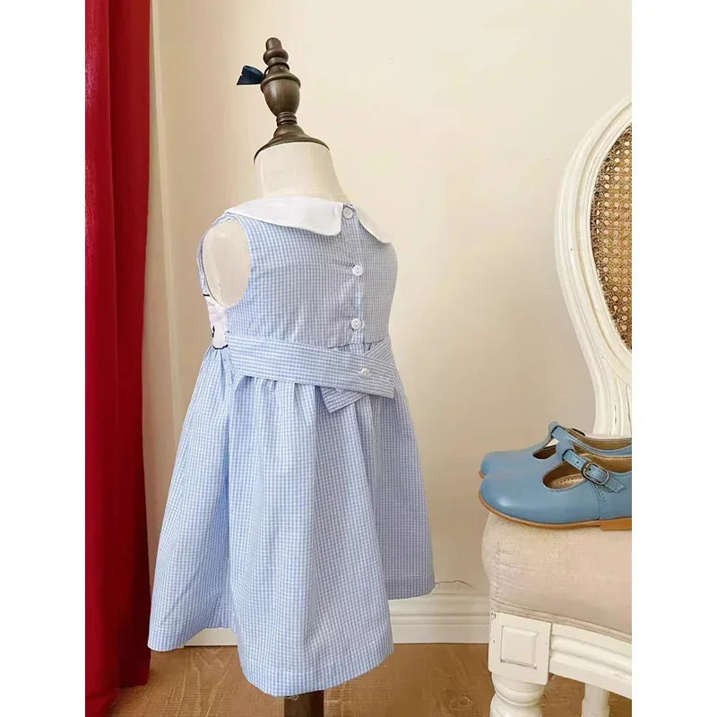 Toddler blue checkered sleeveless dress with white collar displayed on mannequin with blue shoes nearby