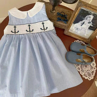 Blue and white embroidered girls party dress with anchor design for toddler girls on table