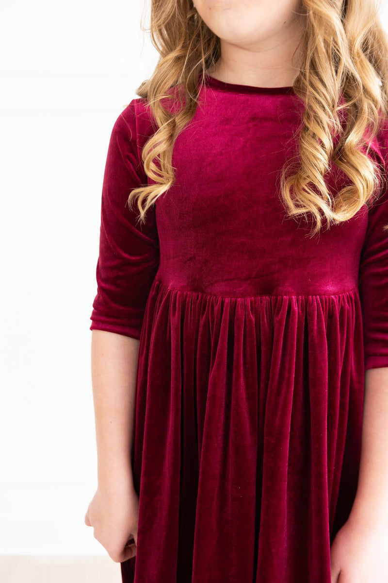 A detailed view of a girl wearing a Cranberry Velvet Twirl Dress from Mila & Rose®, highlighting the elegant velvet texture and charming fit ideal for festive occasions.