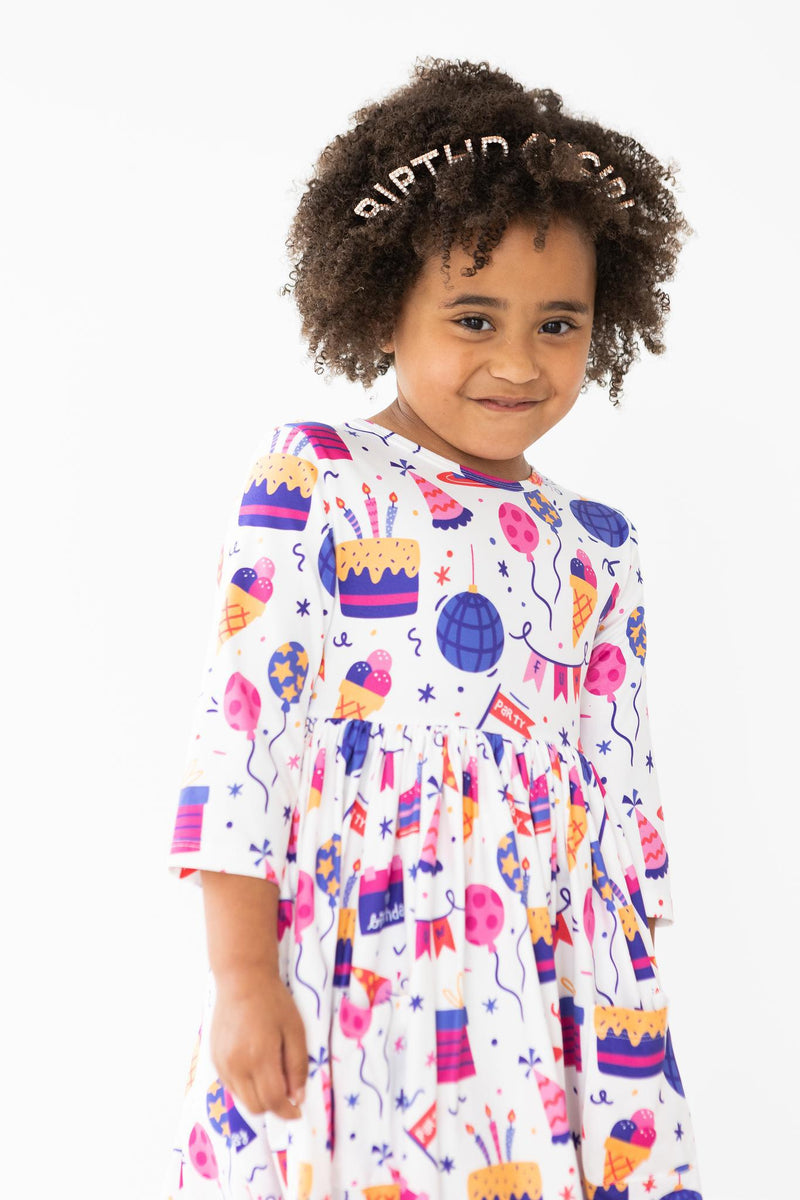 Happy Birthday 3/4 Sleeve Pocket Twirl Dress worn by a cheerful girl with curly hair, radiating birthday fun with colorful festive designs.