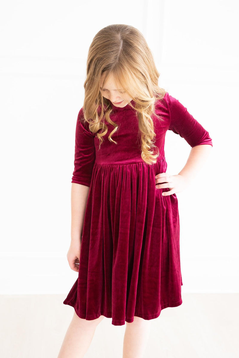 A close-up of a girl in a stunning Cranberry Velvet Twirl Dress from Mila & Rose®, showcasing the dress's soft texture and vibrant color while she strikes a playful pose.