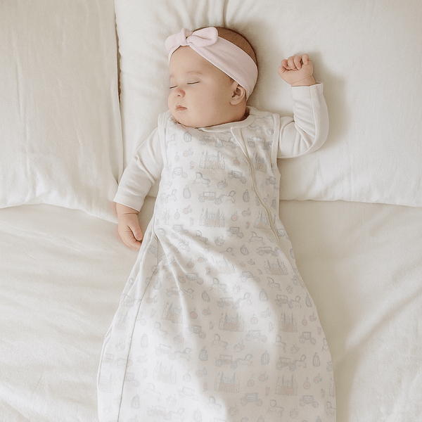 Baby sleeping in a white swaddle with gray patterns on a white couch.