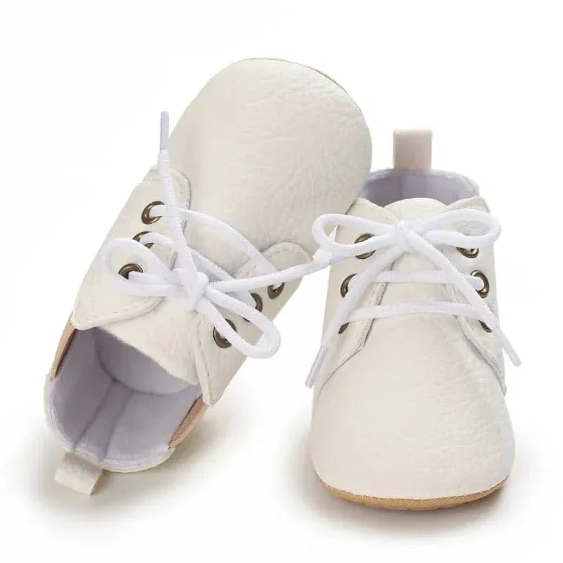 White faux leather baby shoes for infants with laces, displayed side and top view