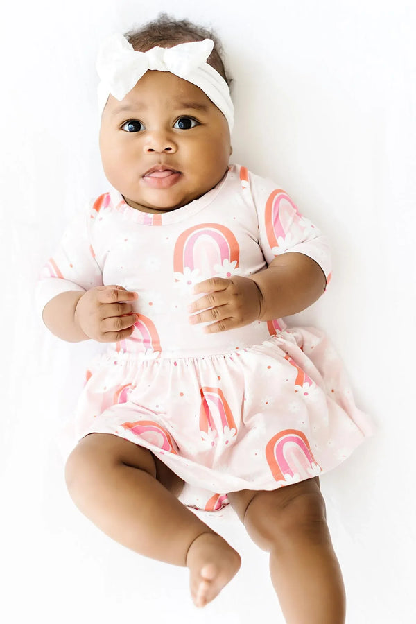 Baby girl wearing pink 3/4 sleeve Twirl Bodysuit with rainbow print and white headband floral baby bodysuit dress