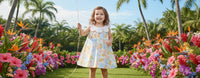 A happy young girl wearing the "Little Selena" A-Line Floral Dress with Petal Collar, holding a balloon amidst a vibrant flower garden, perfect for spring or summer outings.