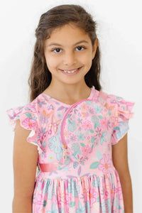 young girl wearing pink floral flutter sleeve twirl dress for girls smiling and standing
