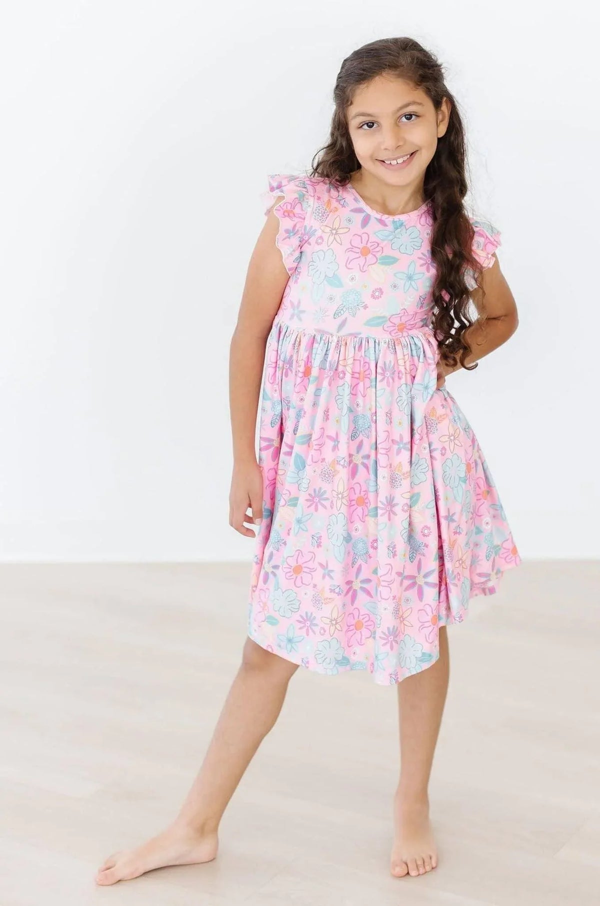 Young girl wearing pink floral flutter sleeve twirl dress for girls smiling and posing barefoot