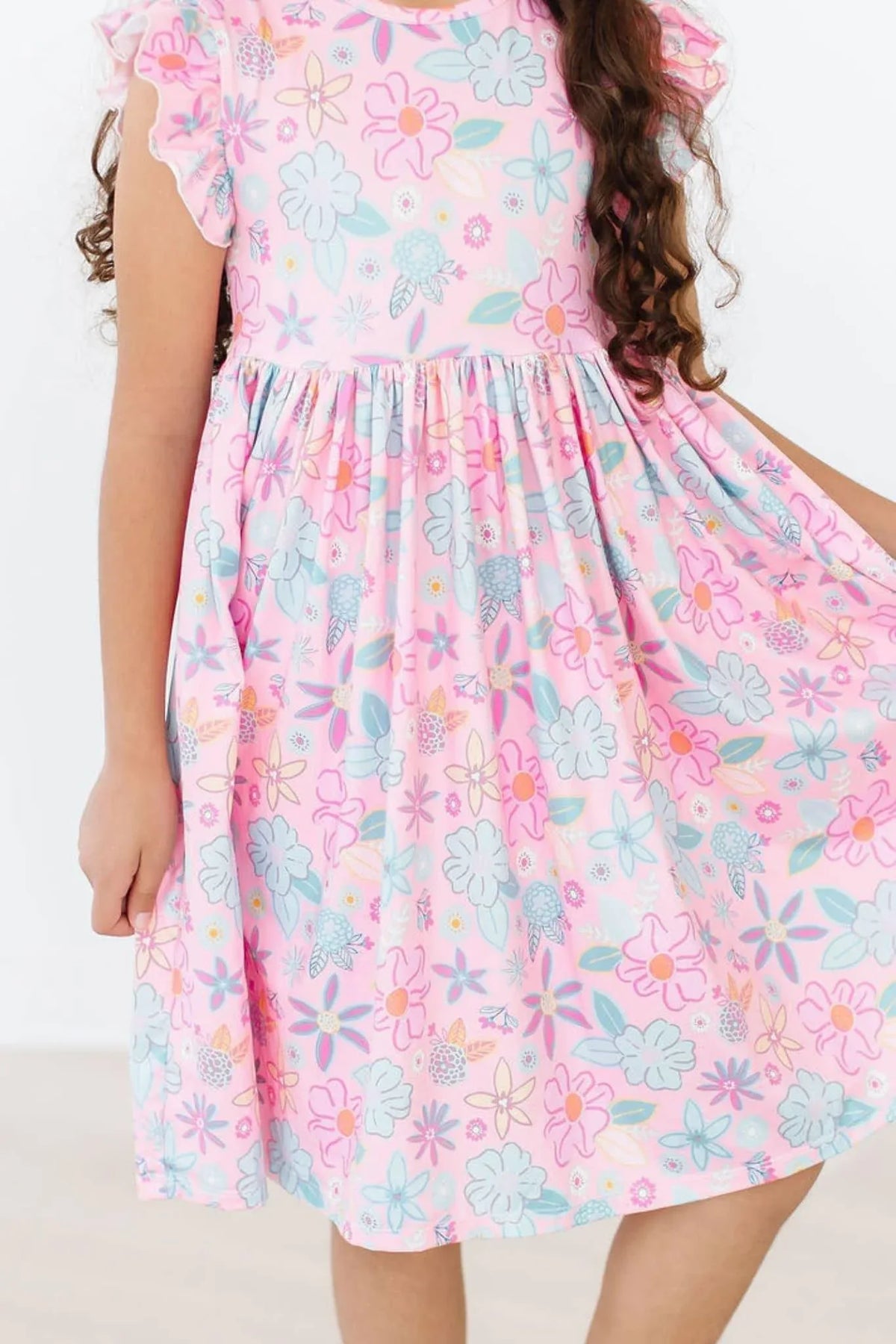 Young girl wearing a pink floral flutter sleeve twirl dress for girls holding the skirt out
