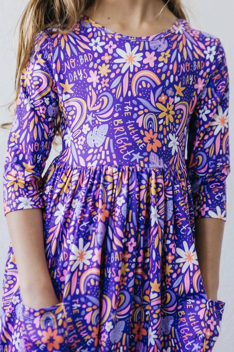 girl wearing purple girls 3/4 sleeve twirl dress with floral and rainbow print standing still