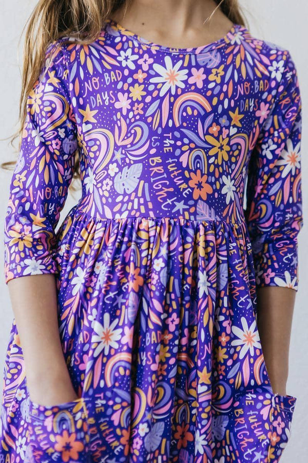 girl wearing purple girls 3/4 sleeve twirl dress with floral and rainbow print standing still