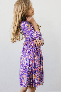 Young girl wearing purple girls 3/4 sleeve twirl dress with floral pattern standing sideways