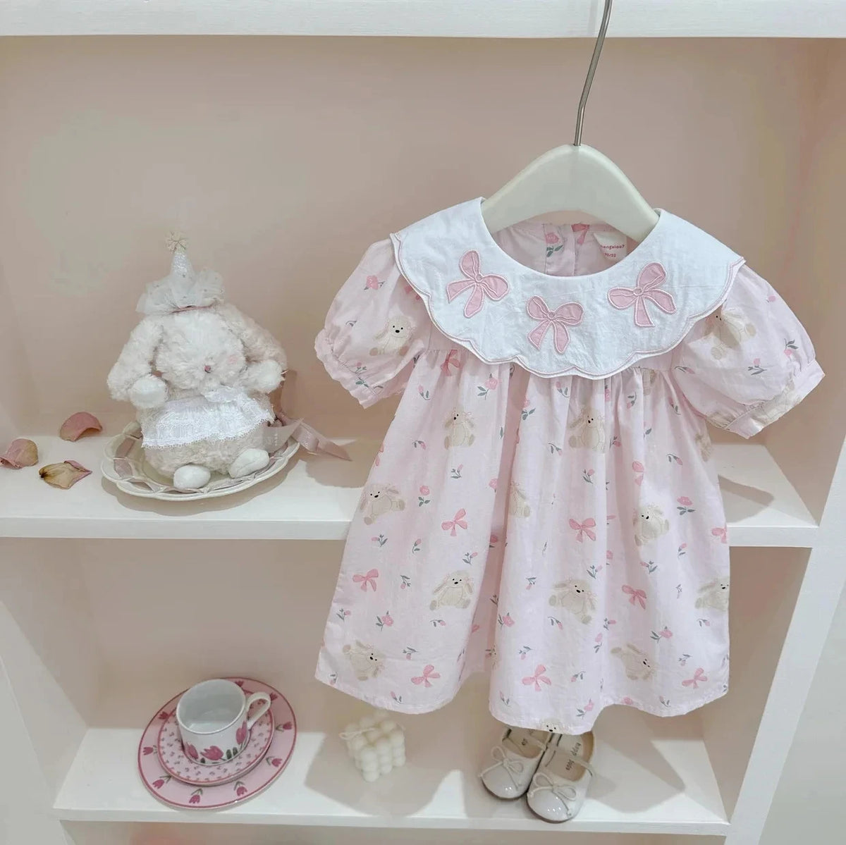 pink girls a-line flower dress for toddlers with embroidered collar on hanger displayed with bunny plush and tea set