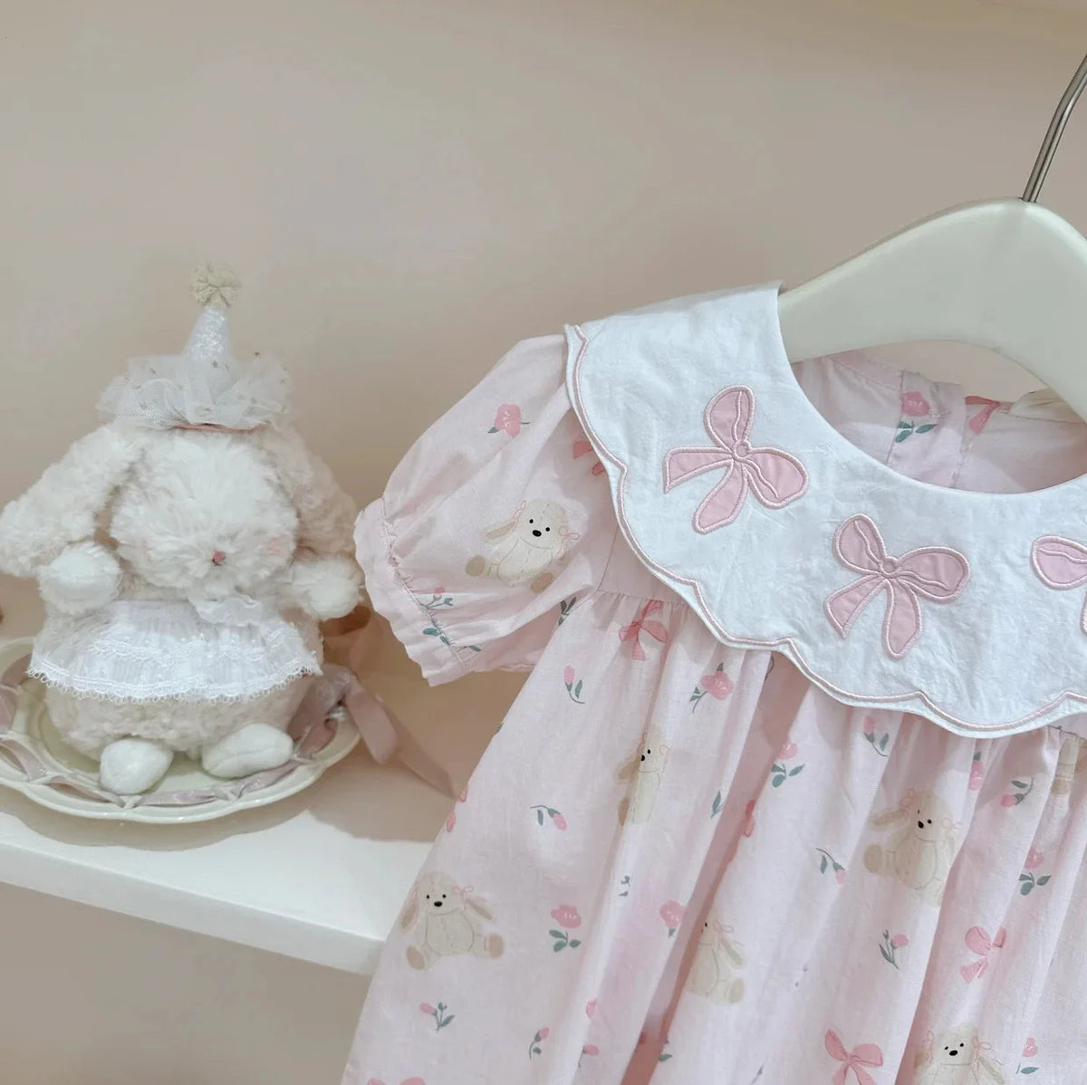 Pink girls a-line flower dress with bows and teddy bear prints hanging on white hanger for baby girls