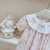 Pink girls a-line flower dress with bows and teddy bear prints hanging on white hanger for baby girls