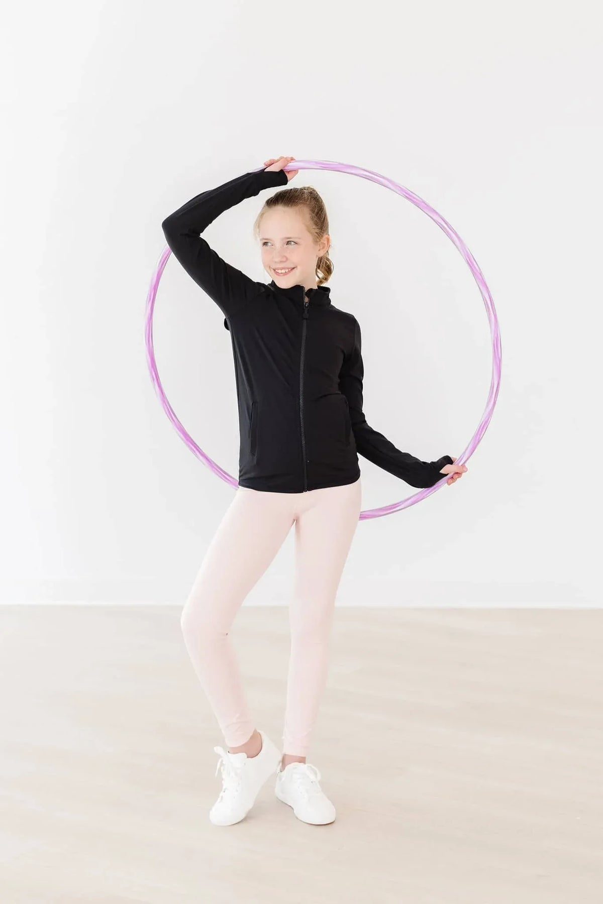 Young girl wearing pink girls active leggings and black jacket posing with a purple hula hoop